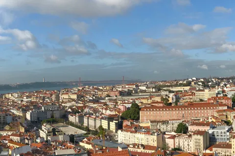 Panoramic daytime view over Lisbon's terracotta rooftops toward the 25 de Abril bridge