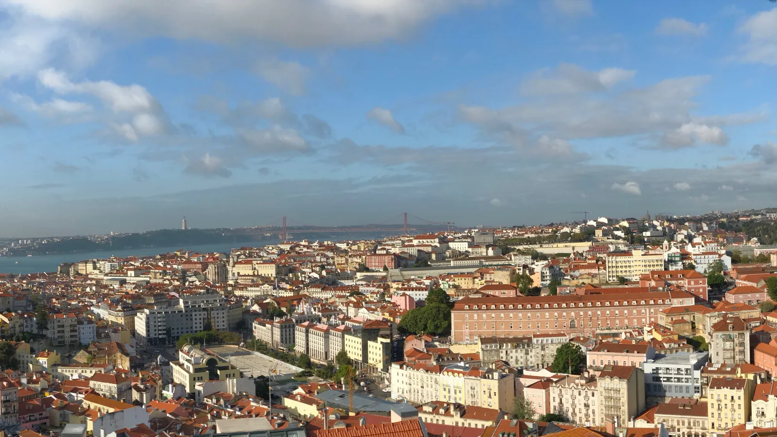 Panoramic daytime view over Lisbon's terracotta rooftops toward the 25 de Abril bridge