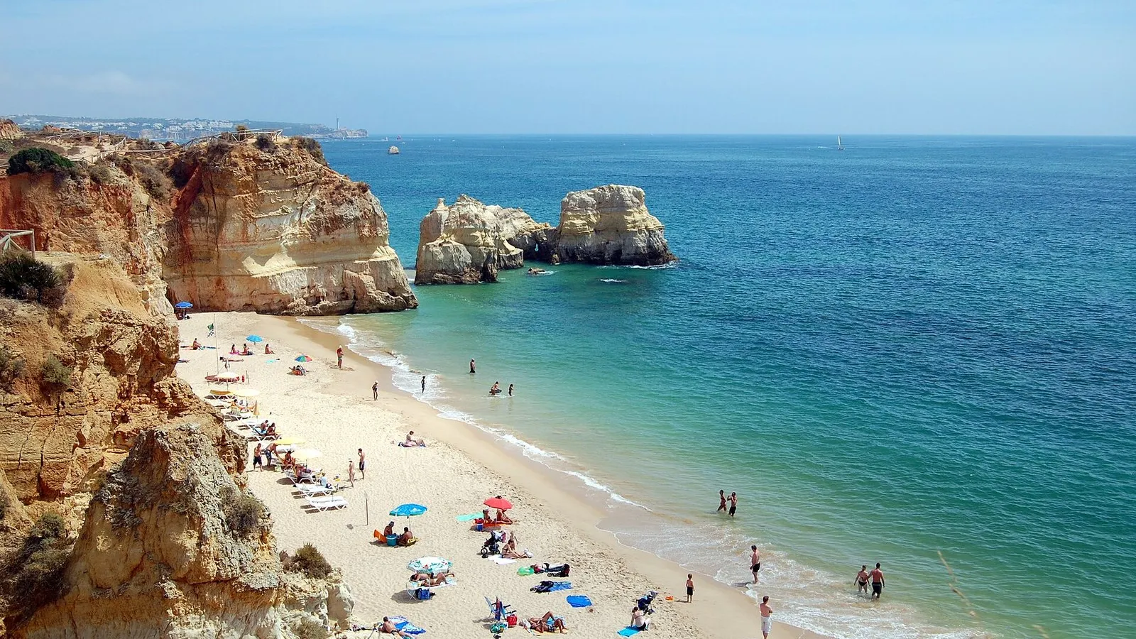 Crowded Algarve beach at Praia da Rocha in Portugal in August, with golden cliffs and turquoise water