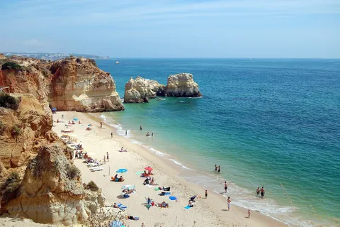 Crowded Algarve beach at Praia da Rocha in Portugal in August, with golden cliffs and turquoise water