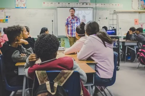 Grupo diverso de estudiantes en pupitres escuchando a un profesor en un aula de colegio internacional