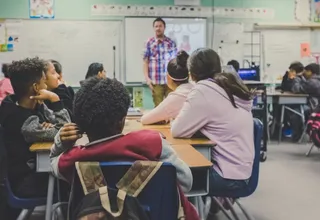 Grupo diverso de estudiantes en pupitres escuchando a un profesor en un aula de colegio internacional