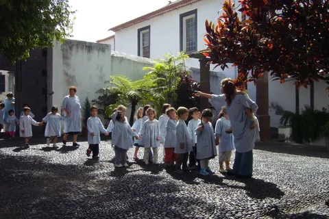 Kindergarten children in matching smocks walk hand in hand with their teachers across a cobbled courtyard in Funchal, Madeira, the kind of group outing typical of daycare in Portugal