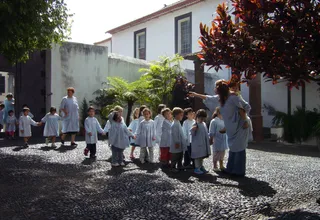 Kindergarten children in matching smocks walk hand in hand with their teachers across a cobbled courtyard in Funchal, Madeira, the kind of group outing typical of daycare in Portugal