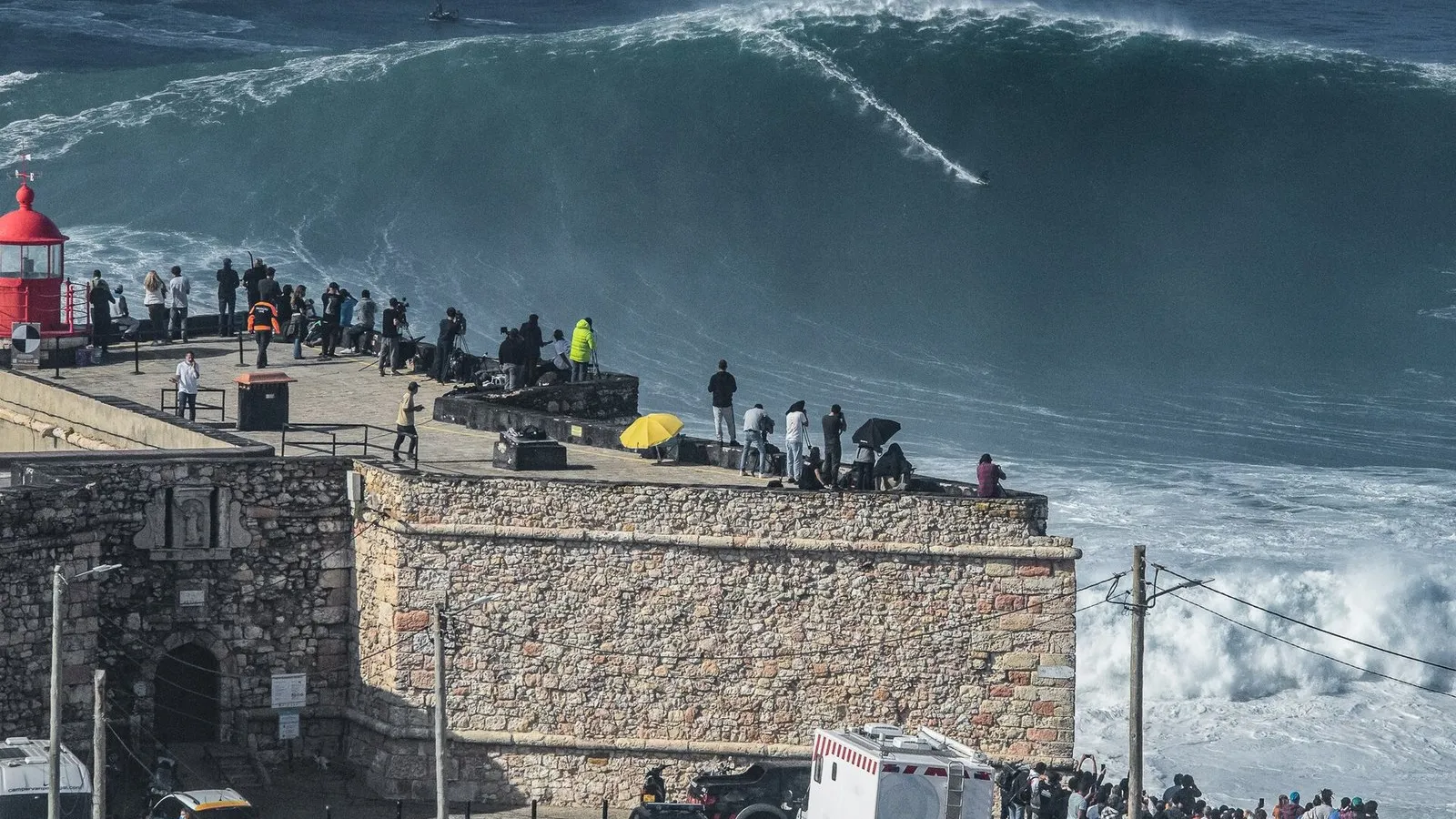 Surfista sobre una ola gigante en Praia do Norte, una de las mejores playas para surfear en Portugal, vista desde el faro-fortaleza de Nazaré