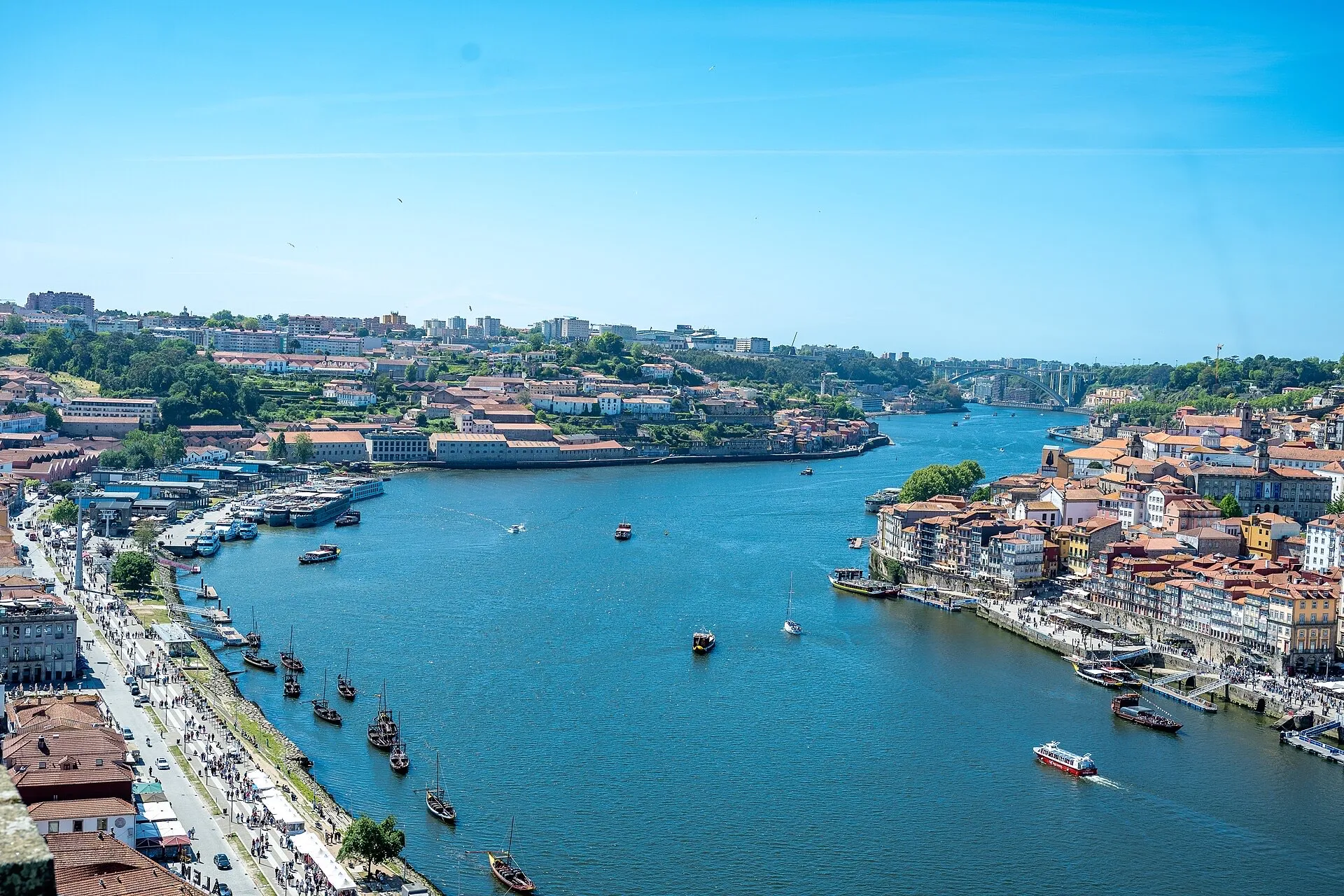 Elevated view up the Douro river in Porto on a sunny day, with rabelo boats, the colourful Ribeira district on the right bank and Vila Nova de Gaia on the left