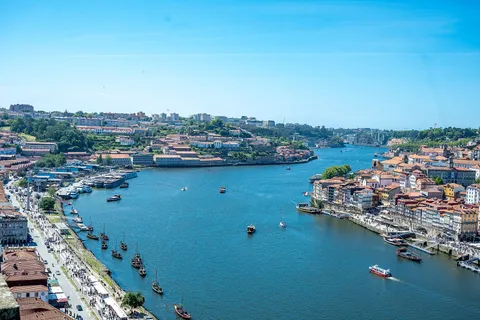 Elevated view up the Douro river in Porto on a sunny day, with rabelo boats, the colourful Ribeira district on the right bank and Vila Nova de Gaia on the left