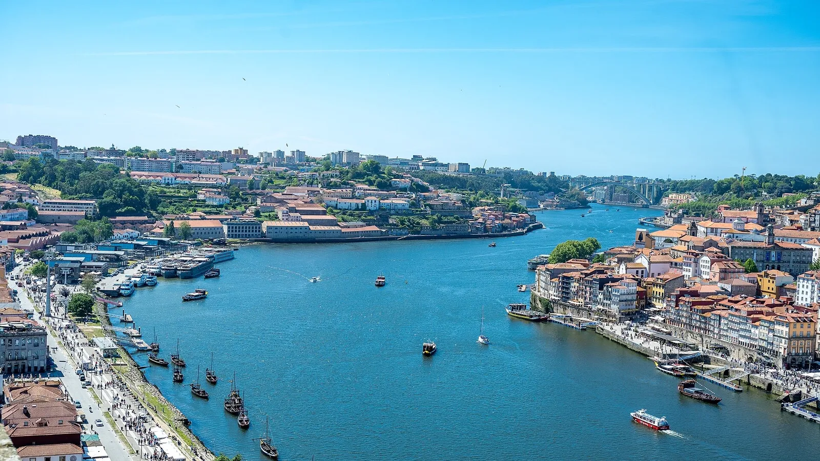 Elevated view up the Douro river in Porto on a sunny day, with rabelo boats, the colourful Ribeira district on the right bank and Vila Nova de Gaia on the left
