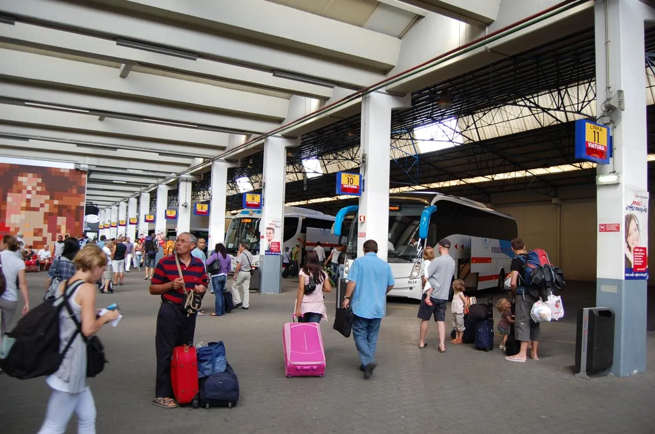 Travellers with rolling suitcases and backpacks wait between coaches at the Sete Rios bus terminal in Lisbon, the kind of arrival day your relocation budget has to cover