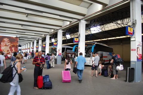 Travellers with rolling suitcases and backpacks wait between coaches at the Sete Rios bus terminal in Lisbon, the kind of arrival day your relocation budget has to cover