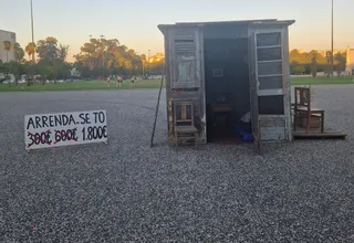 A plywood shack installed as a protest artwork outside the University of Lisbon, with a hand-painted sign reading Arrenda-se T0 and the rent crossed out from 300 to 600 to 1,800 euros, a comment on how hard renting in Portugal has become