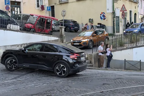 Carros estacionados numa rua de calçada portuguesa em Lisboa, com matrículas portuguesas, ilustrando o que custa comprar um carro em Portugal