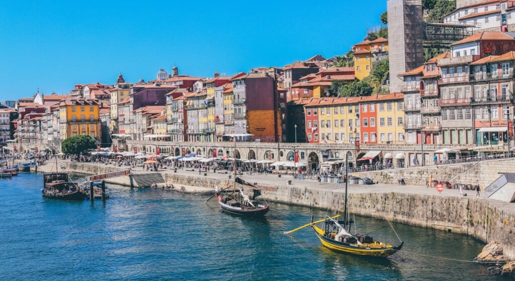 Sunny September afternoon on the Ribeira waterfront in Porto with rabelo boats on the Douro and riverside cafe terraces